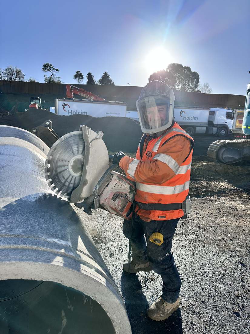 Worker in full face protection cutting concrete pipe